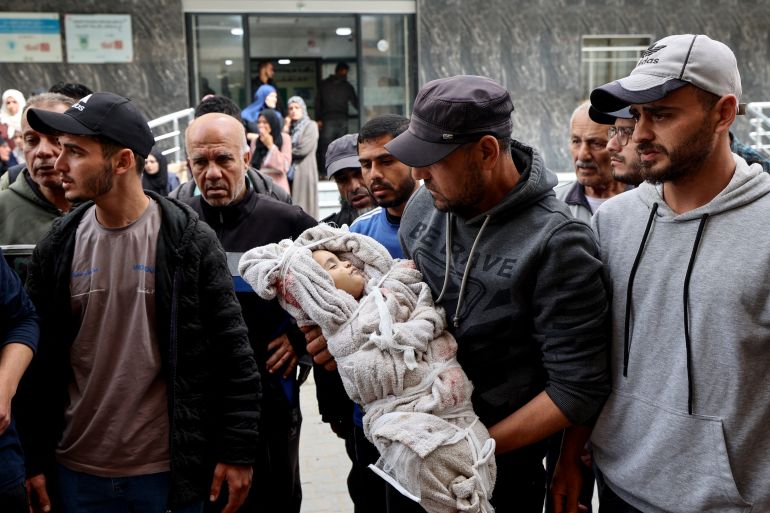 EDITORS NOTE: Graphic content / TOPSHOT - A man carries the shrouded body of Farah Ahmed, who was killed with other members of her family when an Israeli strike hit their home, as he walks outside Al-Awda Hospital in the Nuseirat refugee camp, in the central Gaza Strip on April 30, 2025.