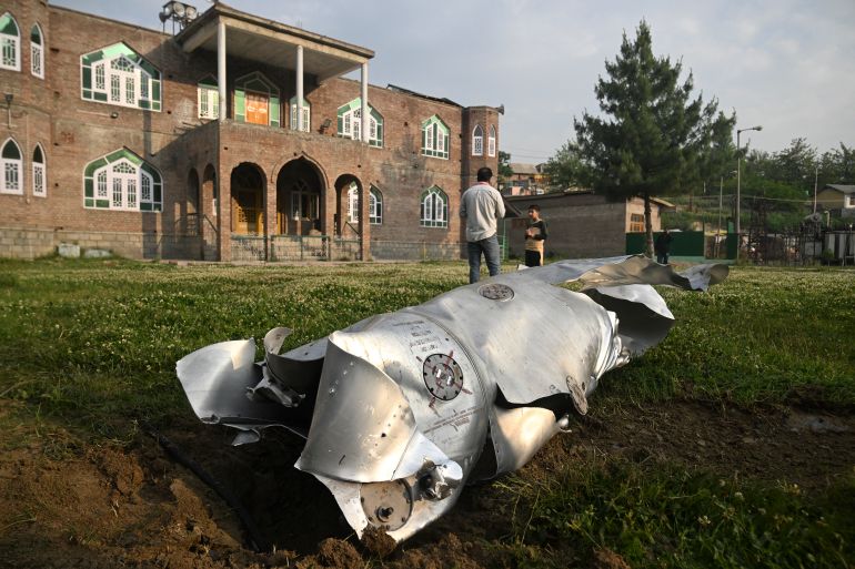 afp_681b03c855ff-1746600904 People stand near a part of an aircraft in Wuyan near Indian-administered Kashmir's main city of Srinagar on May 7, 2025.