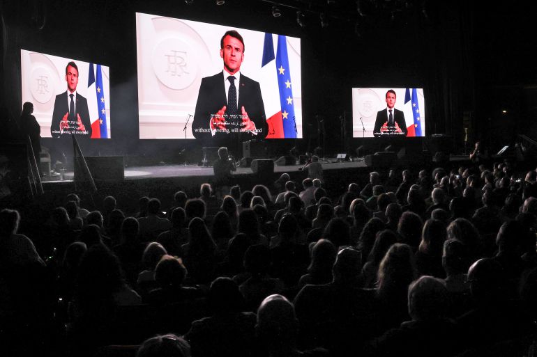 Attendees of the It's Time People’s Peace Summit, listen to a speech by French President Emmanuel Macron, transmitted on large screens at the International Convention Centre in Jerusalem on May 9, 2025.