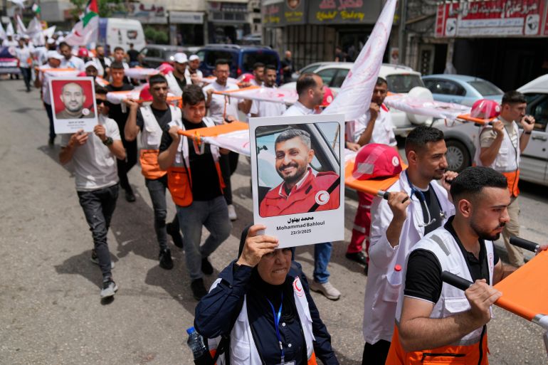 ap_6821de922ecd6-1747050130 A paramedic holds posters with names and pictures of fellow relief workers who lost their lives in the line of humanitarian duty, during a symbolic funeral for 48 fallen Palestinian Red Crescent Society members during the Israel Hamas war in Gaza, according to a PRCS statement, marking the World Day of Red Cross and Red Crescent, in the West Bank city of Ramallah Monday, May 12, 2025. (AP Photo/Nasser Nasser)