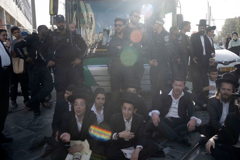 ap_6823497e27528-1747143038 Israeli police stand guard as ultra-Orthodox Jewish men and boys, block a bus from crossing Jaffa Street in central Jerusalem, Thursday, Sept. 29, 2022 to protest attempts to force them to register for Israel's military draft. Military service is mandatory for most Jewish Israeli men, but the ultra-Orthodox often receive exemptions in order to continue their religious studies. (AP Photo/ Maya Alleruzzo)