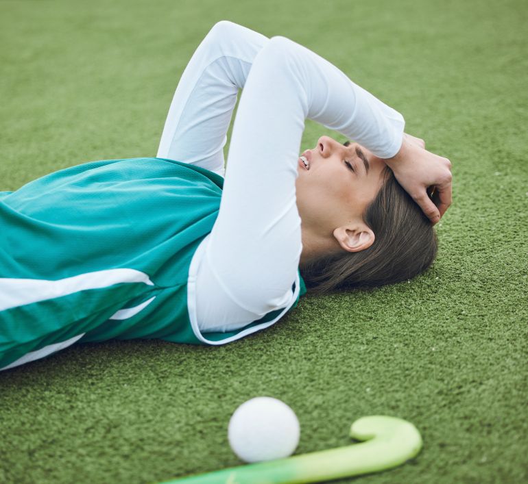 gettyimages-1744747248-1748002554 Hockey player, woman is tired in field with fitness and sport, challenge or loss with burnout outdoor. Exercise, wellness and fatigue with fail in competition, mistake and crisis on stadium turf