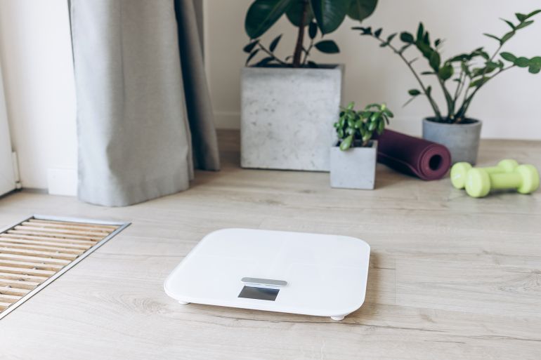 gettyimages-2201664832-1747928474 Fitness equipment and digital scale surrounded by green potted plants on a wooden floor, concept of home exercise and wellness decor - stock photo