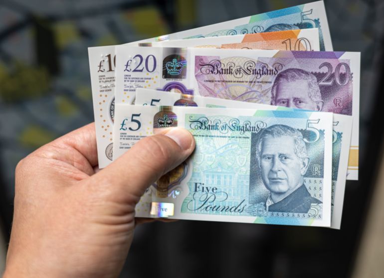 sdfsfsdf2-1747389305 Close-up of a hand holding British pound banknotes (£5, £10, £20), featuring King Charles III. Useful for finance, banking, currency exchange, and economic themes