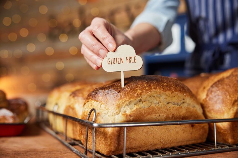 Sales Assistant In Bakery Putting Gluten Free Label Into Freshly Baked Baked Sourdough Loaves Of Bread; Shutterstock ID 1911997906; purchase_order: aj; job: ; client: ; other: