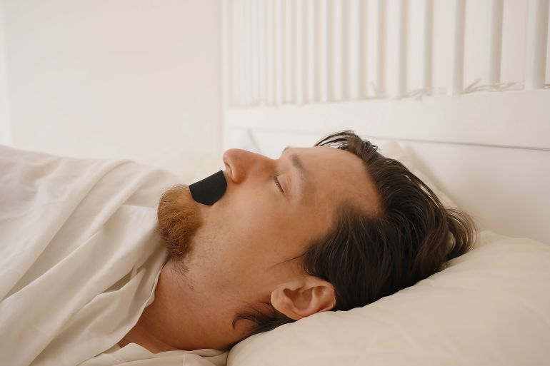 shutterstock_2609823061-1748111502 Man Sleeping on His Back with Black Mouth Tape in Bright White Bedroom, Nose Breathing and Anti Snoring Concept; Shutterstock ID 2609823061; purchase_order: ajj; job: ; client: ; other: