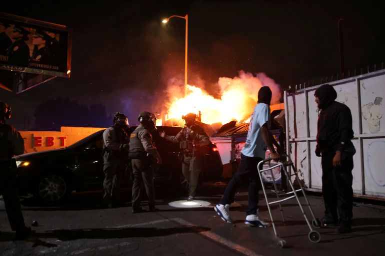 A man looks back at a fire after law enforcement helped him out of a car during a protest in Compton, Calif., Saturday, June 7, 2025, after federal immigration authorities conducted operations. (AP Photo/Ethan Swope)