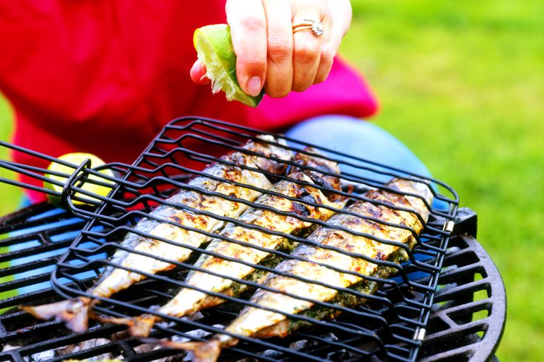 Lime being squeezed over mackerel on barbecue - stock photo
