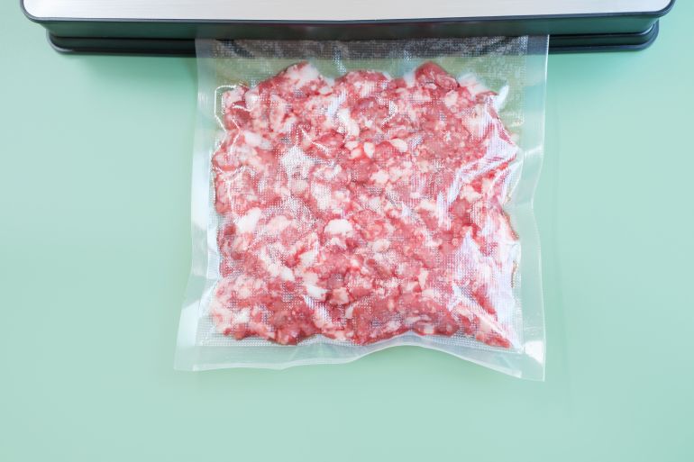 Minced meat in a vacuum bag on a green background close up.