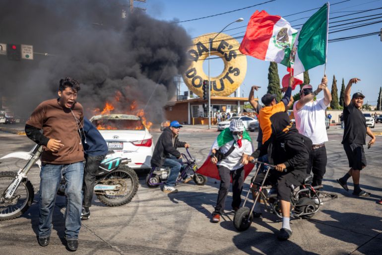 People congregate in an intersection as a car burns, during a standoff by protesters and law enforcement following multiple detentions by Immigration and Customs Enforcement (ICE), in the Los Angeles County city of Paramount, California, U.S., June 7, 2025. REUTERS/Barbara Davidson