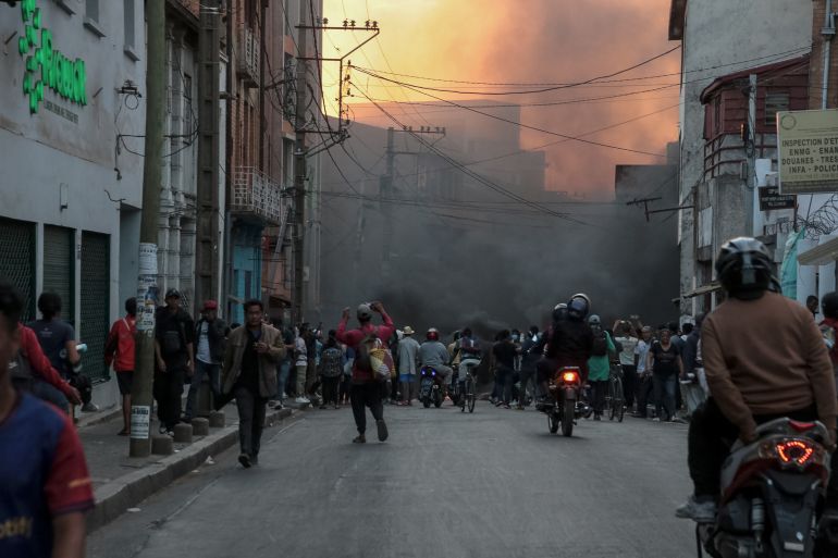 Protesters gather near a plume of smoke as they demonstrate against repeated water and electricity outages in Antananarivo on September 25, 2025.
