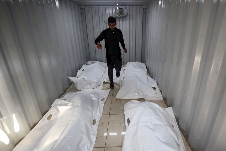 A man walks among body bags laid down inside a prefabricated structure outside the al-Awda hospital in the Nuseirat refugee camp in the central Gaza Strip, following an Israeli strike on September 27, 2025.