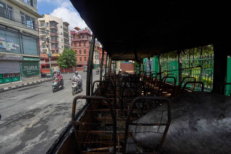 ap_68c5bbf58ba9e-1757789173 Nepalese people drive past a bus burnt during anti-corruption protests sparked by a short-lived social media ban in Kathmandu, Nepal, Saturday, Sept. 13, 2025. (AP Photo/Niranjan Shrestha)