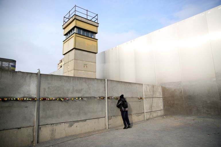 BERLIN, GERMANY - NOVEMBER 09: Visitors peek through slats at a still-standing portion of the Berlin Wall at the Berlin Wall memorial in Bernauerstrasse on the 35th anniversary of the fall of the Wall on November 09, 2024 in Berlin, Germany. The Berlin Wall, built by the communist authorities of East Germany in 1961, separated East and West Germany during the Cold War. Its breach as part of the mostly peaceful 1989 revolution was among the most significant and symbolic events of the revolutions that led to the disintegration of the Soviet-dominated East Bloc and the end of communist hegemony in the region. (Photo by Maryam Majd/Getty Images)