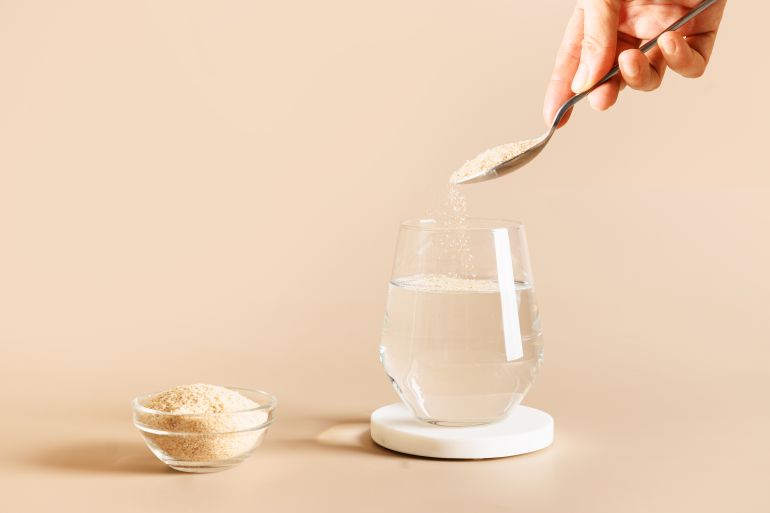 gettyimages-1364416271-1757950882 Woman adds psyllium fiber to glass of water on beige background. Superfood for healthy intestines and gluten free diet.