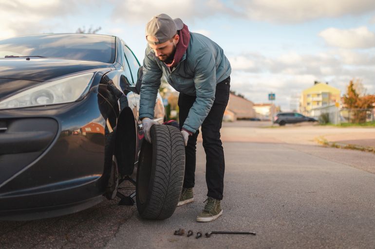 Young man changing tires on his car outdoors. He is preparing for winter time.