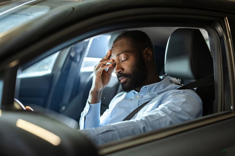 gettyimages-2201933622-1758383473 A man inside a vehicle appears tired and stressed, with his hand on his head. Reflects fatigue, busy schedules, and the challenges of everyday transportation.
