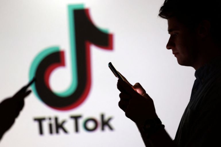 Teenagers pose for a photo while holding smartphones in front of a TikTok logo in this illustration taken September 11, 2025. REUTERS/Dado Ruvic/Illustration