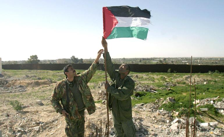 Two Palestinian policemen install a flag next to the Egyptian border (in the background) in the southern Gaza Strip city of Rafah 28 January 2005. Some 2,000 Palestinian security forces were deployed in southern Gaza today with orders to prevent rocket attacks as Israeli Prime Minister Ariel Sharon said he detected an