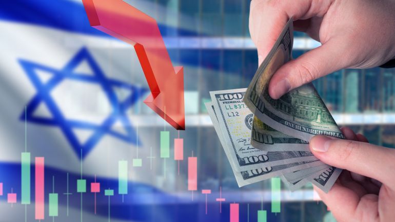 shutterstock_2397367713-1758471105 Business in Israel. Money in hands of man. Flag of Israel. Down arrow metaphor for crisis. Investment chart. Problems in Israeli economy concept. Problems for business from Israel. إسرائيل اقتصاد بورصة أسهم تصنيف
