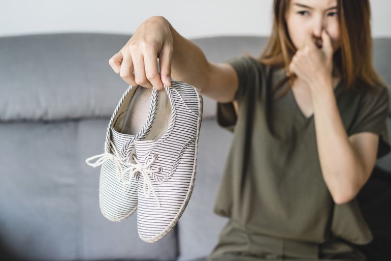 567trfh-1759416593 Young asian woman holding a pair of smelly and stinky shoes at home
