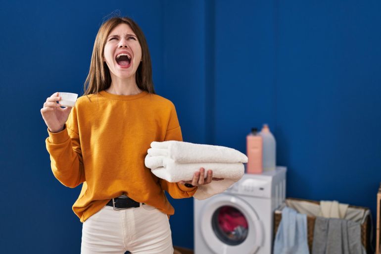 5d981d984d98a5-1759683165 Young brunette woman holding detergent and clean laundry angry and mad فري بيك