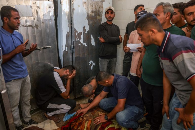 afp_68dcf1f49538-1759310324 EDITORS NOTE: Graphic content / Palestinian men surround the bodies of people killed in Israeli strikes, at the morgue of al-Aqsa Martyrs hospital in Deir el-Balah in the central Gaza Strip, on October 1, 2025.