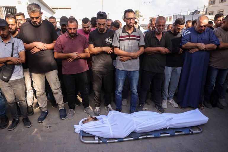 afp_68dcf20faf6c-1759310351 Palestinians pray over the body of a man killed in an Israeli strike, before a funeral procession outside al-Aqsa Martyrs hospital in Deir el-Balah in the central Gaza Strip, on October 1, 2025.