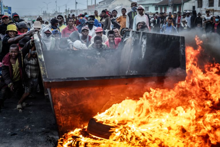 TOPSHOT - Protesters react as they push a metal container to use as a barricade during clashes with Malagasy security forces amid a strike calling for constitutional reforms and the resignation of President Andry Rajoelina in Antananarivo, on October 9, 2025.