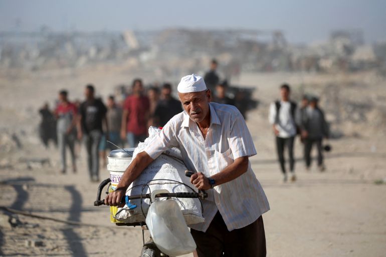 A Palestinian man pushes his bike as he and others make their way to Gaza City through the so-called "Netzarim corridor" from Nuseirat in the central Gaza Strip on October 11, 2025.