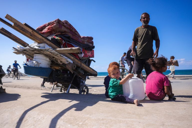 A Palestinian man rests with his children as he, along with others, makes his way along Al-Rashid road toward Gaza City from Nuseirat in the central Gaza Strip on October 10, 2025.
