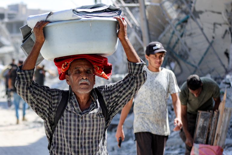 A man walks with a basin on his head loaded with canvases past destroyed buildings in the centre of Khan Yunis in the southern Gaza Strip on October 10, 2025, as displaced people return to their homes after Israeli forces' withdrawal.