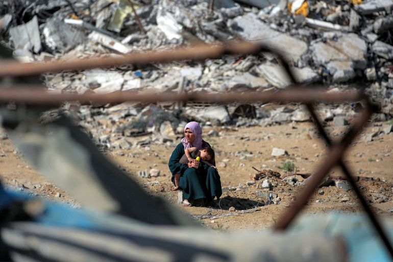 A woman sits with a child before a mound of rubble on the road to Gaza City near Nuseirat in the central Gaza Strip on October 10, 2025.