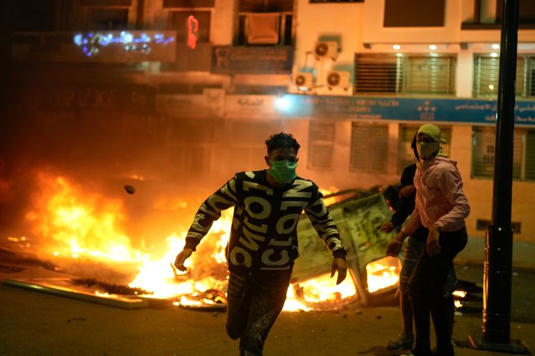 ap_68de022e8d8c2-1759380014 A person runs past a torched police vehicle as youth led protests calling for healthcare and education reforms turned violent, in Sale, Morocco, Wednesday, Oct. 1, 2025. (AP Photo/Mosa'ab Elshamy)