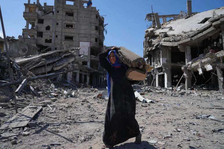An elderly displaced Palestinian woman carries an item past destroyed buildings in Khan Younis, southern Gaza Strip, Friday, Oct. 10, 2025, after Israel and Hamas agreed to a pause in their war and the release of the remaining hostages. (AP Photo/Jehad Alshrafi)