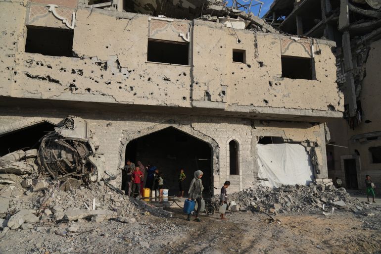 ap_68f493895e4ce-1760859017 Displaced Palestinians collect water from a destroyed building in Khan Younis, Gaza Strip, Saturday, Oct. 18, 2025. (AP Photo/Jehad Alshrafi)