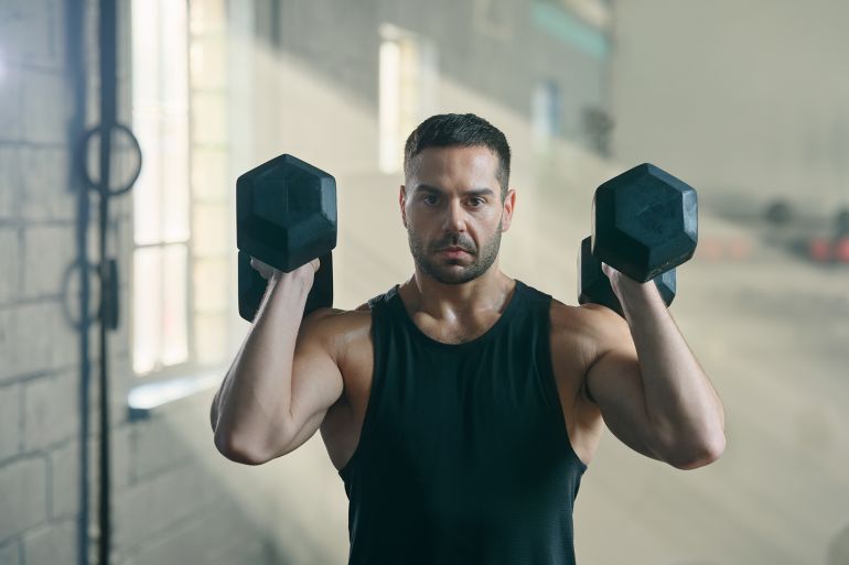 gettyimages-2207771482-1760720876 Young white man lifting heavy dumbbells as part of weight training in cross training gym, weights, exercising, physical activity
