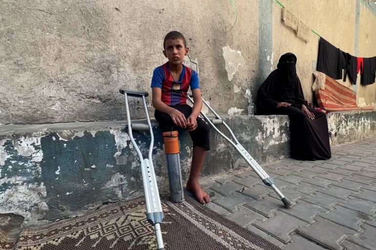 طفل الفلسطيني راتب أبو قليق على عكازين، يجر أنبوبا بلاستيكيا ثبته مكان ساقه المبتورة، يتخذه بديلا بدائيا عن طرف صناعي