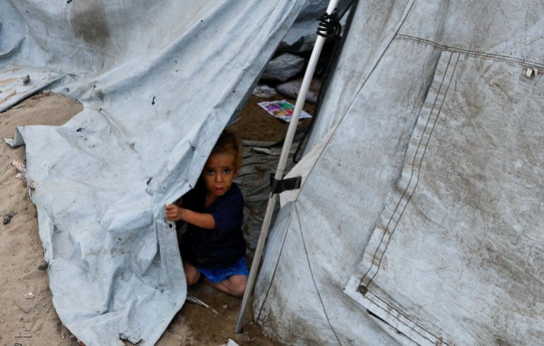 A displaced Palestinian girl looks out from inside a tent, amid a ceasefire between Israel and Hamas, in the central Gaza Strip, October 12, 2025. REUTERS/Mahmoud Issa