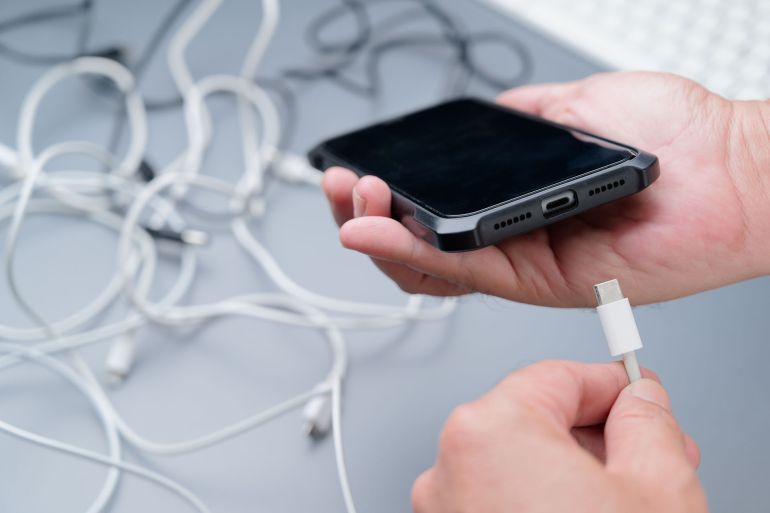 Hand holding a wrong type of electric charging cables before charging the phone battery, with confused usb wires on the table; Shutterstock ID 2527780949; purchase_order: AJA; job: ; client: ; other: