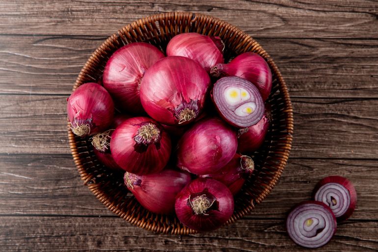 Top view of basket full of whole and cut red onions on wooden background فري بيك
