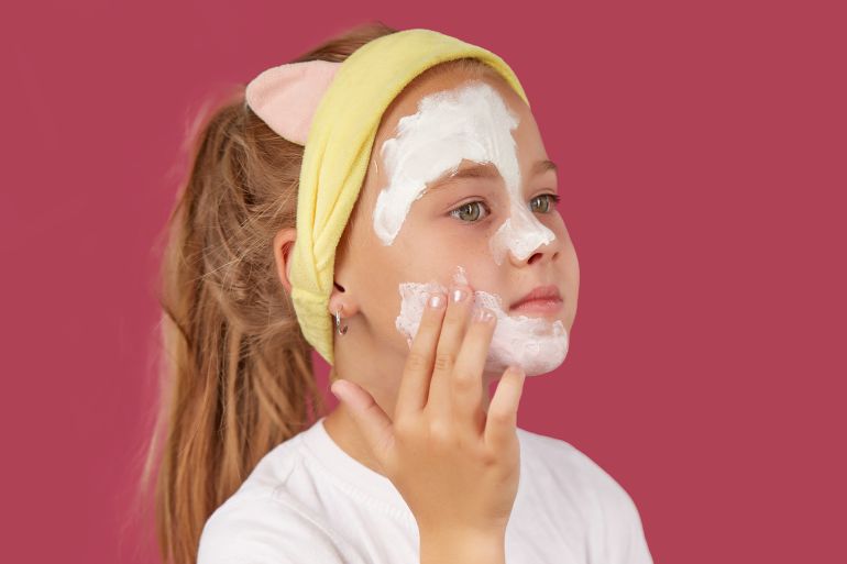 A little girl puts on a cosmetic mask on an isolated red background. by Юрий Дровнин ادوبي ستوك