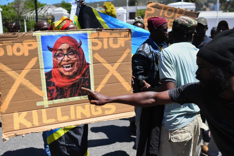 afp_690c8d716d03-1762430321-1 Protesters hold a placard with a picture of the augmented face of Tanzanian President Samia Suluhu Hassan, during a picket where about 50 Tanzanians living in Cape Town protested against the recent actions by the Tanzanian government during their presidential election, outside the South African Parliament in Cape Town on November 5, 2025.