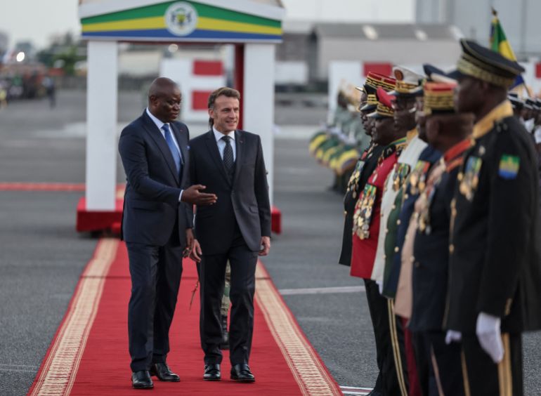 afp_6923d8ddd0a2-1763956957 TOPSHOT - Gabon's President Brice Oligui Nguema (L) and France’s President Emmanuel Macron (2nd L) inspect the guard of honour upon Macron's arrival at the Leon-Mba International Airport in Libreville on November 23, 2025. (Photo by Ludovic MARIN / AFP)