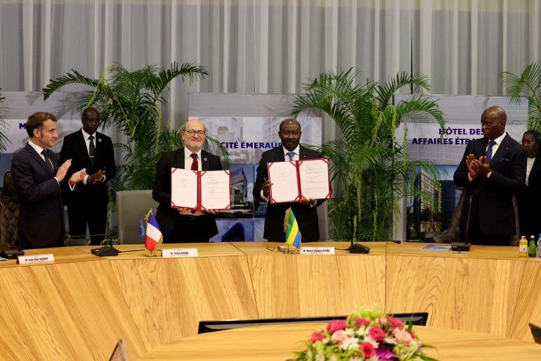 afp_6923d915cb50-1763957013 Gabon's Economy minister Henri-Claude Oyima (2nd L) and France's Chief Executive Officer of Agence Française de Developpement (AFD - French Development Agency) Remy Rioux (2nd L) pose after signing a contract on a railway planned reconstruction, as Gabon's President Brice Oligui Nguema (R) and France's President Emmanuel Macron (L) attend following their meeting in Libreville on November 23, 2025. (Photo by Ludovic MARIN / AFP)