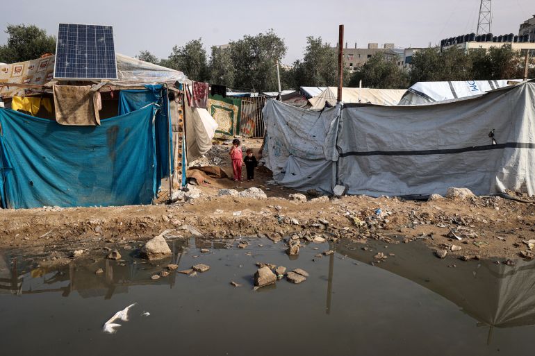 afp_692c035210dd-1764492114 TOPSHOT - Children stand amid makeshift shelters at the Nuseirat camp for displaced Palestinians in the central Gaza Strip on November 29, 2025.