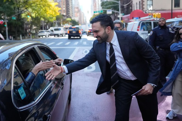 ap_69084c203041c-1762151456 New York City mayoral candidate Zohran Mamdani greets some people in a car while surrounded by reporters in New York, Monday, Oct. 27, 2025. (AP Photo/Seth Wenig)