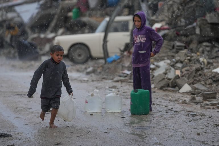 ap_69197bccc80cb-1763277772 A barefoot boy walks in the rain carrying a plastic jerrycan of water in the Sheikh Radwan neighborhood of Gaza City, Friday, Nov. 14, 2025. (AP Photo/Jehad Alshrafi)