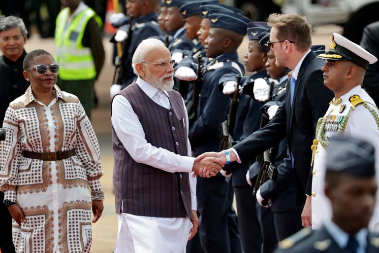 ap_692069fc6295a-1763731964 Indian Prime Minister Narendra Modi, center, is welcomed on his arrival at the Air Force Base Waterkloof, near Pretoria, South Africa, Friday Nov. 21, 2025, ahead of the G20 Summit. (Kim Ludbrook/Pool Photo via AP)