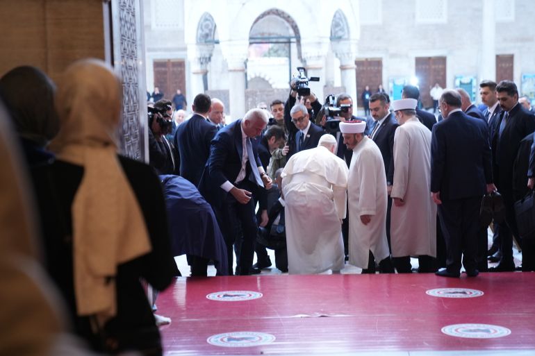 ap_692b027177f4e-1764426353 Pope Leo XIV, center, puts his shoes back on after visiting the Ottoman-era Sultan Ahmed or Blue Mosque, in Istanbul, Turkey, Saturday, Nov. 29, 2025. (AP Photo/Domenico Stinellis)